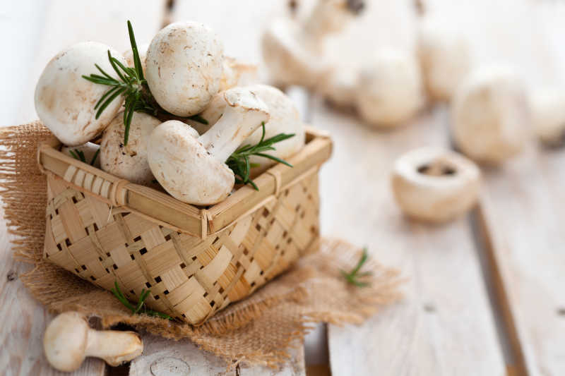 木质桌板上散落的白色香菇和篮子里溢满的香菇迷迭香