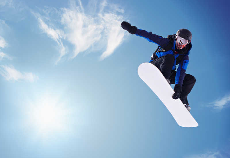 蓝天阳光下跳跃而起的单板滑雪运动员