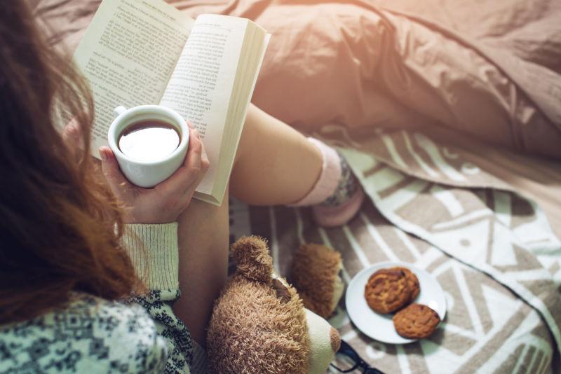 躺在床上看书的女孩穿着温暖的袜子喝咖啡