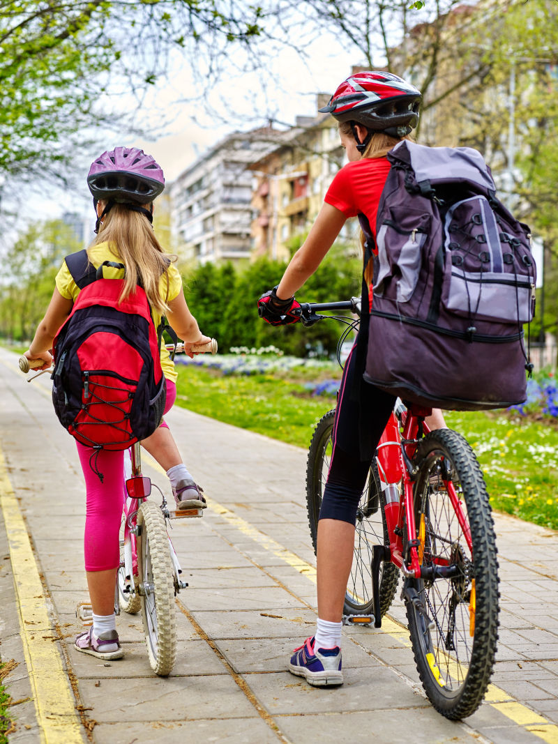 骑自行车的女孩戴着自行车头盔和玻璃背着帆布包的自行车女童骑自行车