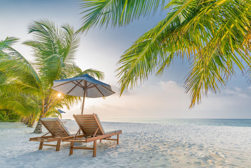 暑假背景-热带海滩上两个躺椅和太阳伞的浪漫日落景色