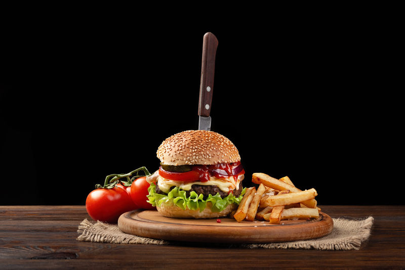 自制汉堡特写镜头与牛肉-西红柿-生菜-奶酪和炸薯条在砧板上-在汉堡里
