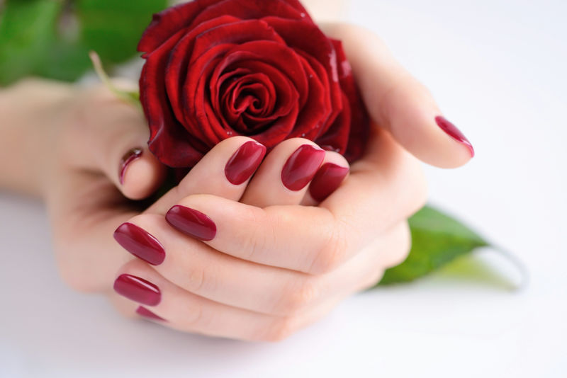 一个女人的手拿着红色的指甲和一束红玫瑰.