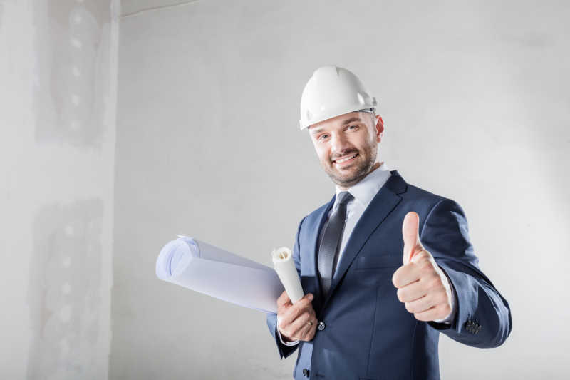 抱着图纸面带微笑举着大拇指的人