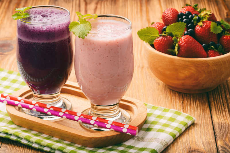 健康的牛奶鸡尾酒草莓和蓝莓在棕色的木制背景上