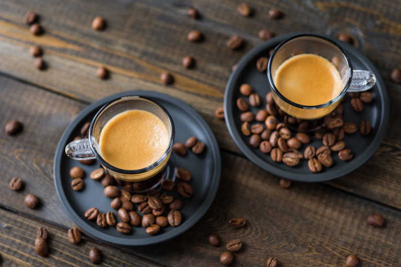 放在木桌上的两杯意大利浓咖啡和咖啡豆