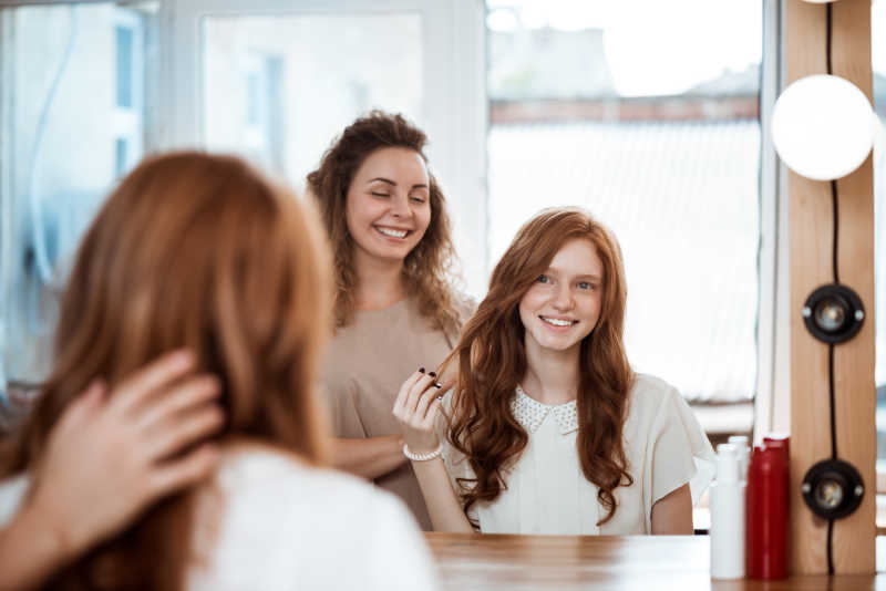 女理发师和微笑着女孩在美容院照镜子