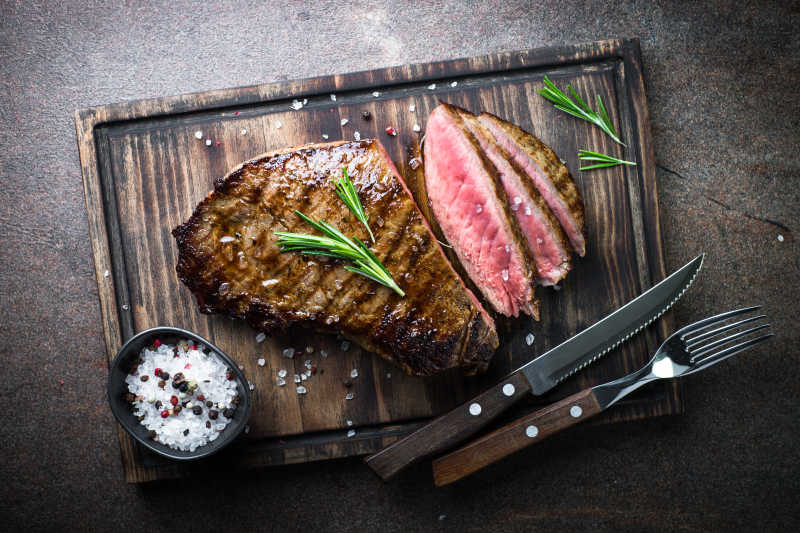 切开的牛排和刀叉摆在木盘上