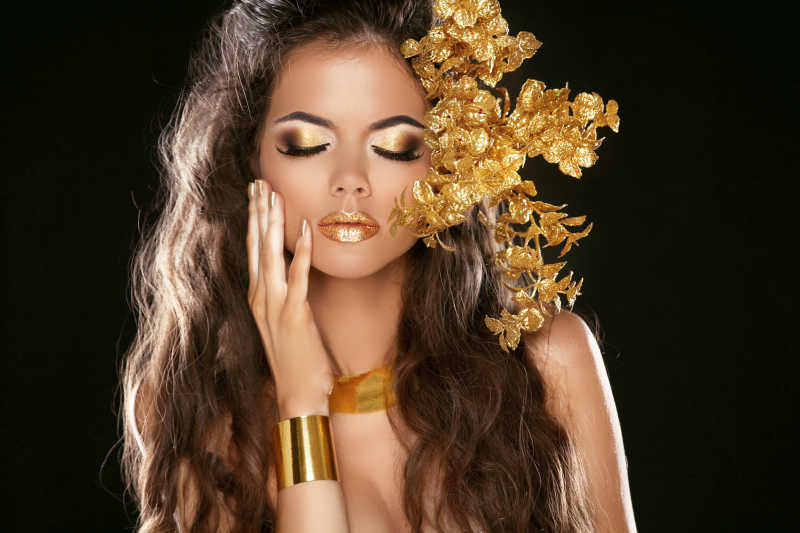 黑色背景下的时尚美女的金色的妆容和黄金首饰