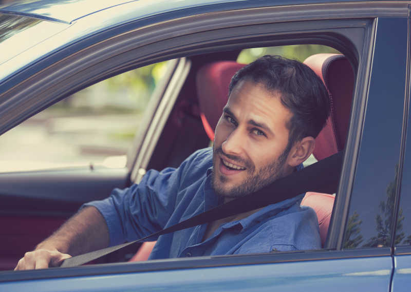 一名男司机面带微笑的坐在车内系安全带