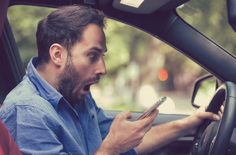 一个男人坐在车上吃惊的看着手机