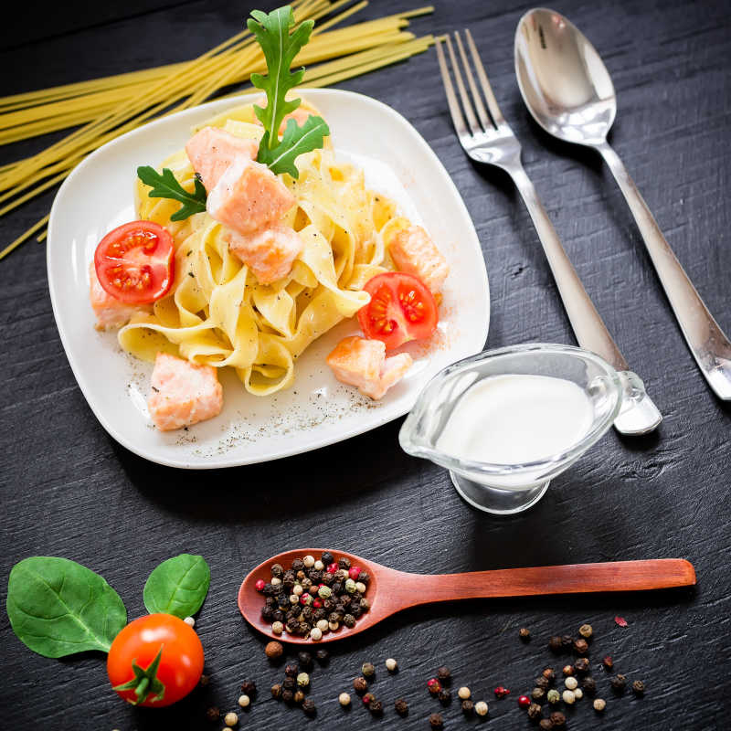 深色餐桌上准备开吃的番茄鲑鱼意大利面和沙司及调味料