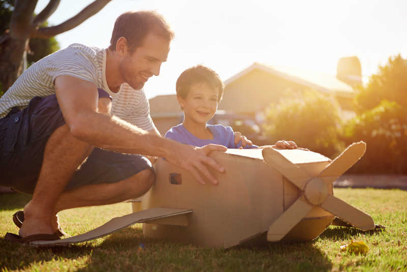 儿子和爸爸在草地上玩纸板做的飞机