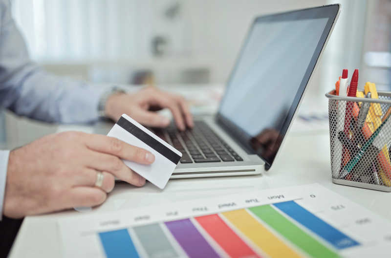 拿着信用卡在笔记本电脑上付款