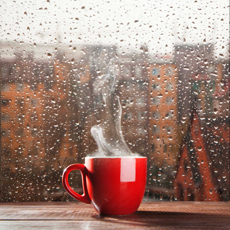 在雨天窗口背景下红色的咖啡杯