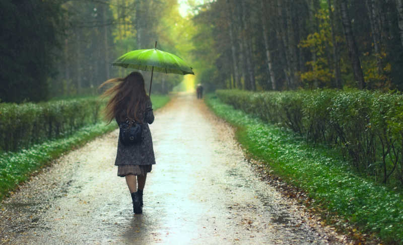 女孩打着伞走在雨中小径的路上