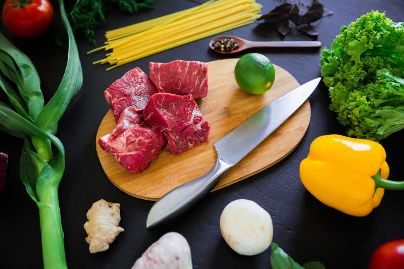 在深色背景下的砧板上的生肉刀意大利面和新鲜蔬菜