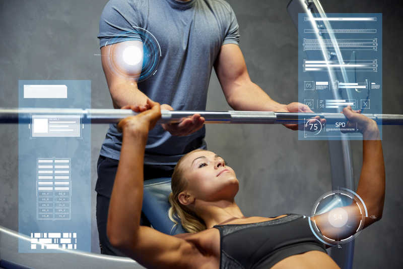 健身房里教练帮女性利用杠铃健身