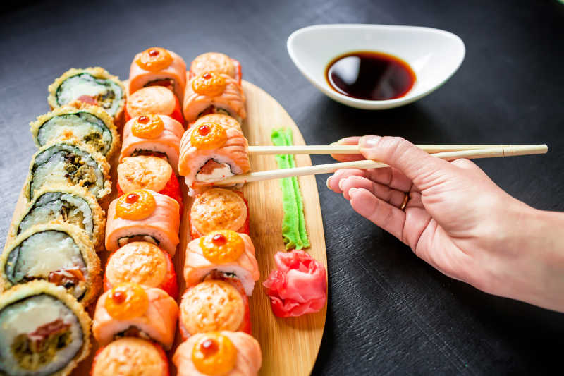 寿司卷酱芥末和女孩手用筷子在深色背景上