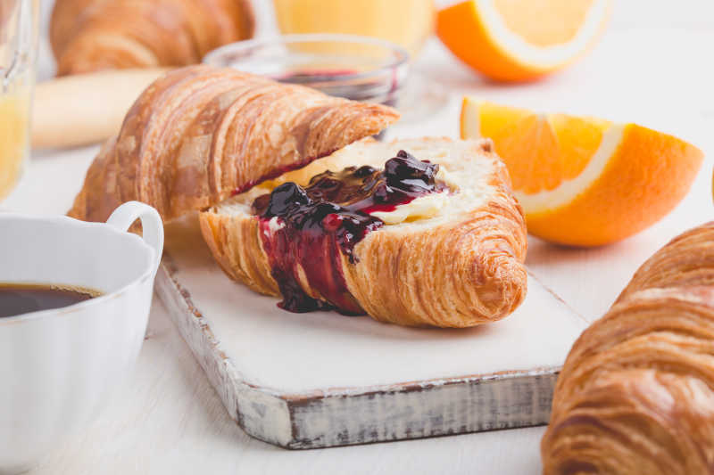 白色的木制背景下的羊角面包果酱橙汁和咖啡