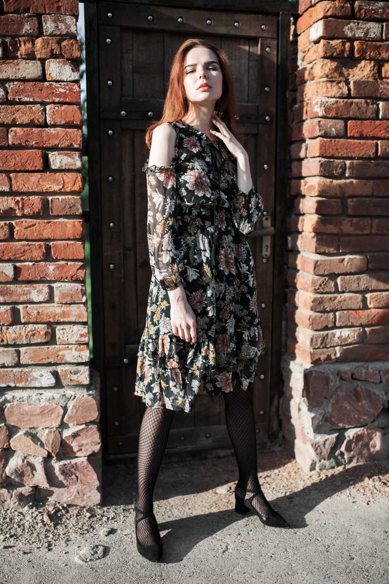 时尚的女孩穿着碎花连衣裙站在墙边