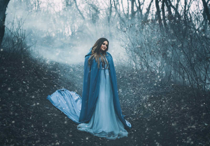 穿着蓝色雨衣的女性站在森林雾里