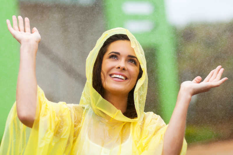 穿着黄色雨衣的女性在下雨天里开心的笑着