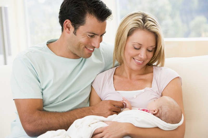 夫妻在客厅里微笑的看着怀里的婴儿