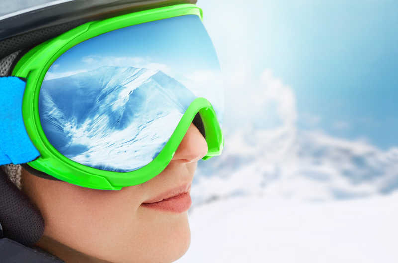 冬季在滑雪场滑雪板滑雪的年轻女孩和护目镜倒映的雪山