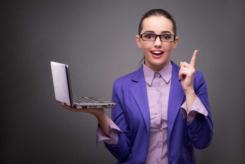 灰色背景上的女商人手拿笔记本电脑高兴的竖着手指