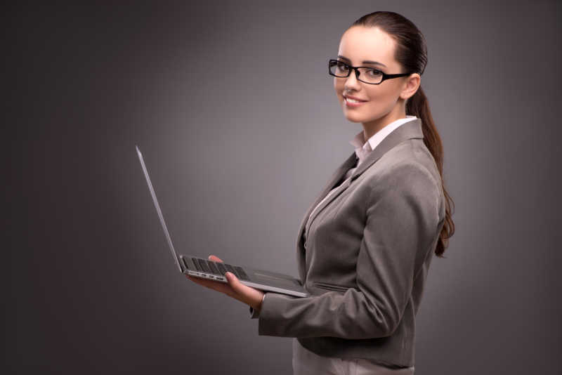 灰色背景上的拿着笔记本电脑的女商人