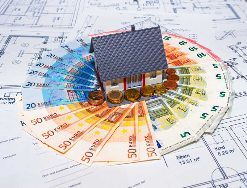 纸片上摆放整齐的欧元纸币硬币和房屋模型