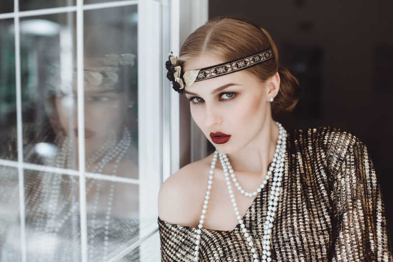 靠在墙边的带有珍珠项链的时尚女子