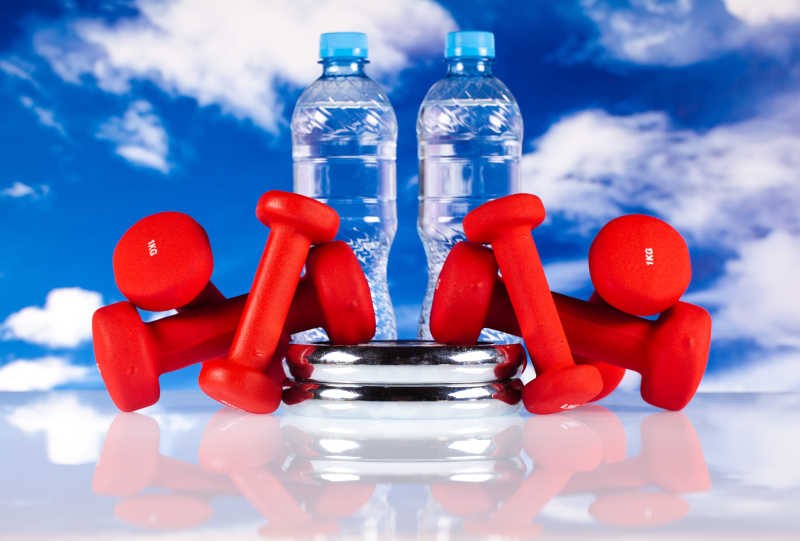 蓝天背景下的两瓶水和红色的哑铃