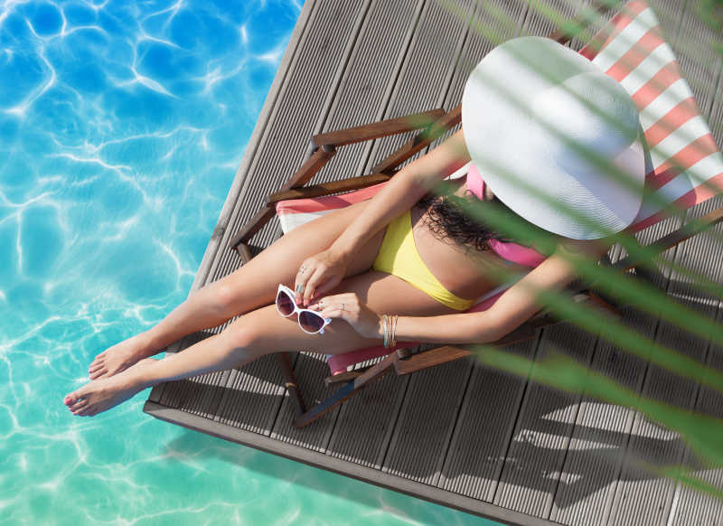 游泳池上躺在沙滩椅上的比基尼美女