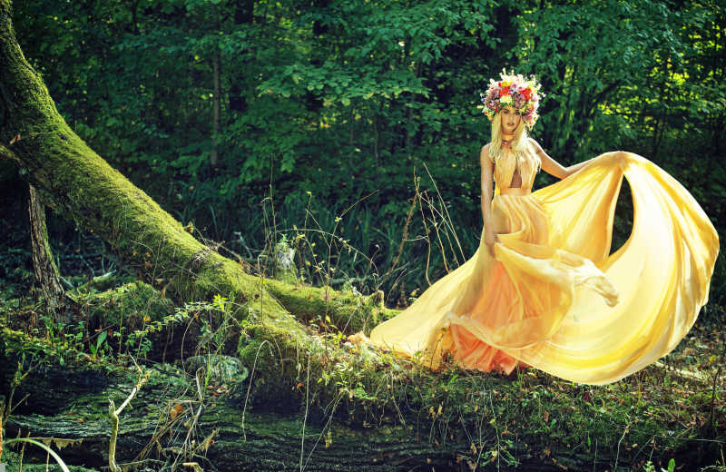 带有美丽花环的金发模特站在森林阳光下