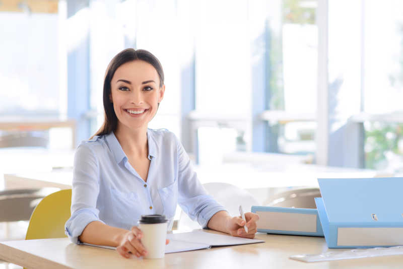 坐在桌子旁的工作的女商人喝着咖啡
