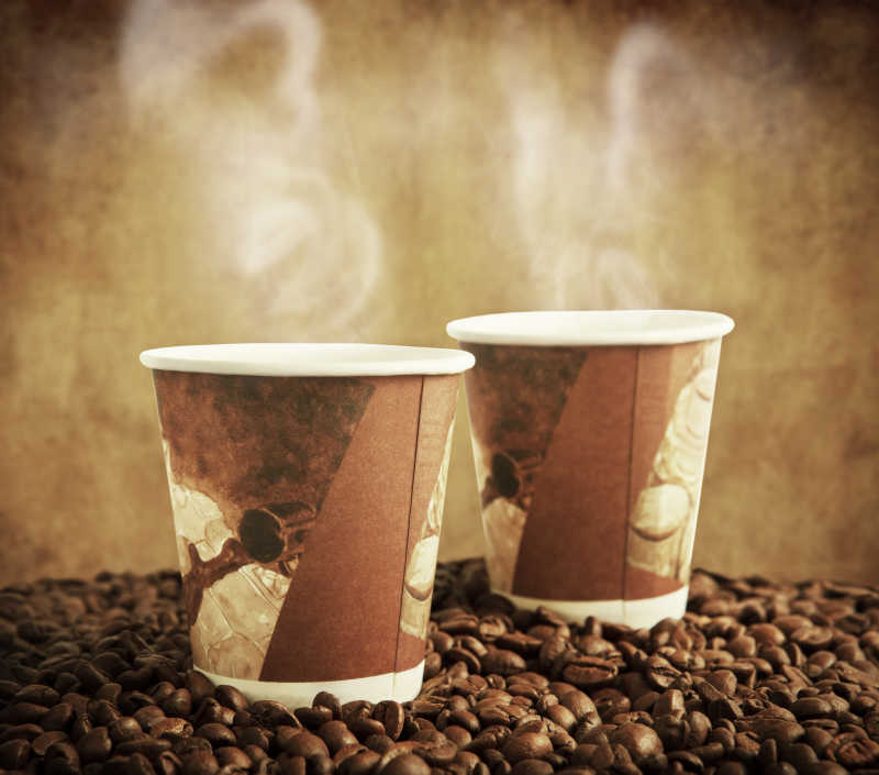咖啡豆上的两杯装有热咖啡的纸杯