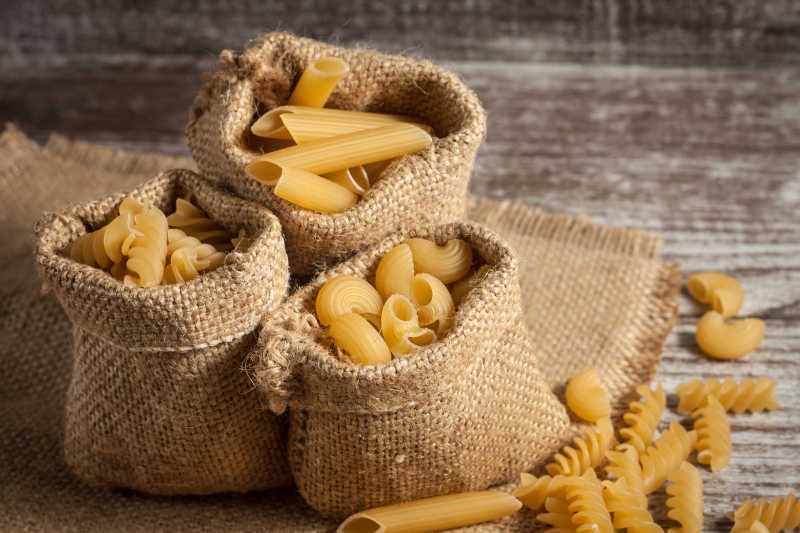 木制背景上的小麻袋里的不同类型的意面