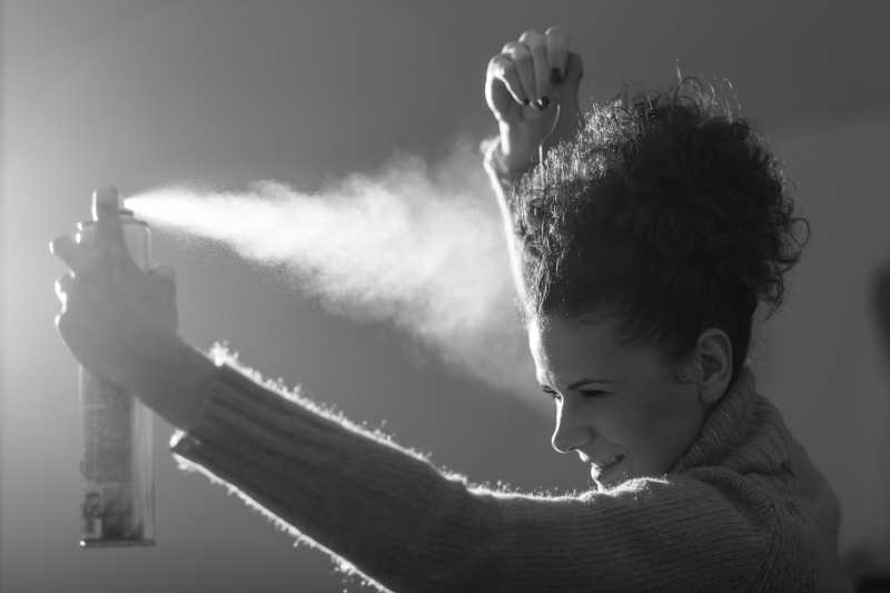 年轻的女孩喷发胶固定她的发型特写