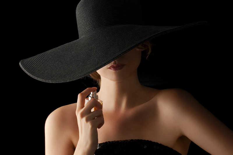 黑色背景帽子的优雅女人喷香水特写