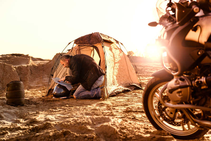骑摩托车骑手在帐篷里检查他的旅行地图