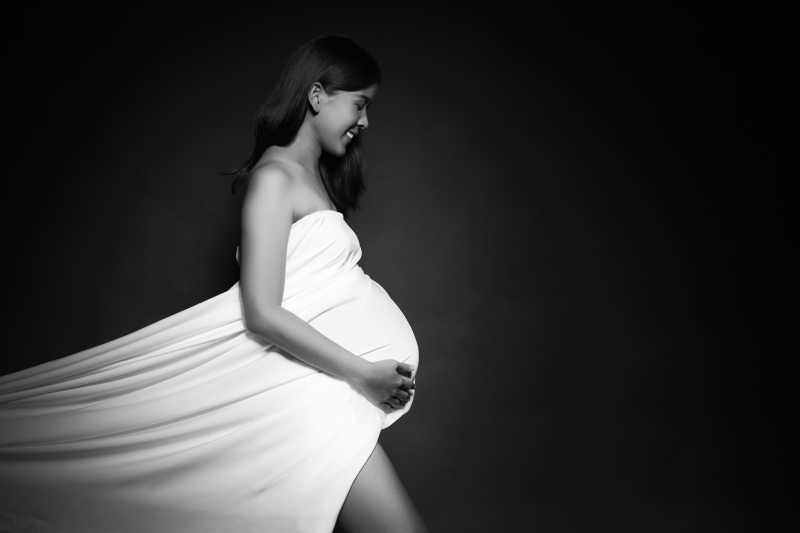 年轻孕妇的在黑色背景上穿的白色纱裙