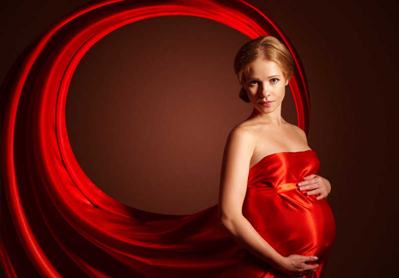 红色丝绸连衣裙的美丽的孕妇的艺术肖像
