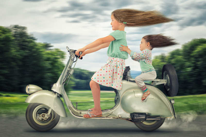 两个坐在电瓶车上的小女孩头发被吹直创意特写