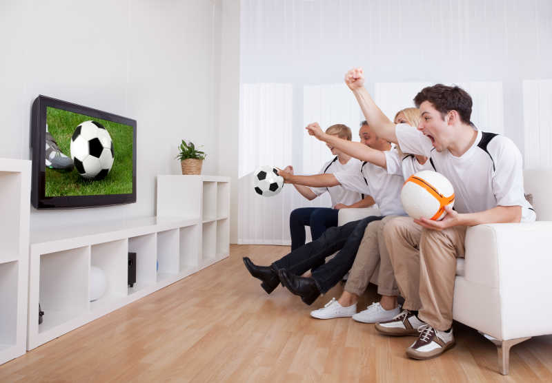 足球迷坐在沙发上看着电视里播放的足球赛