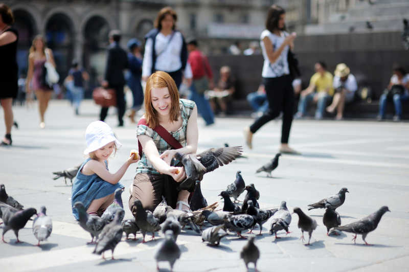 在广场中心喂鸽子的母女