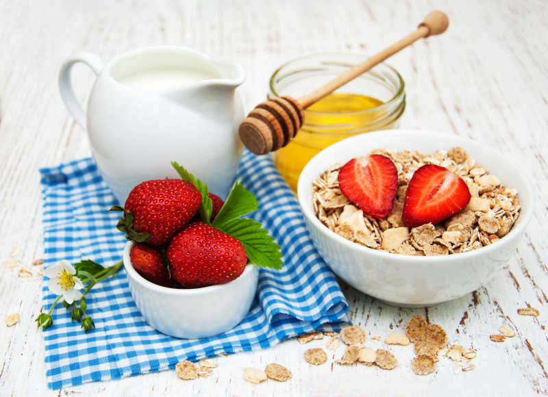 木制背景蓝布牛奶草莓蜂蜜和点缀着切开草莓的麦片