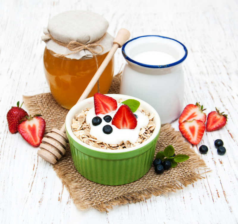 木制背景没开封的蜂蜜和一罐牛奶一碗带有浆果点缀的麦片