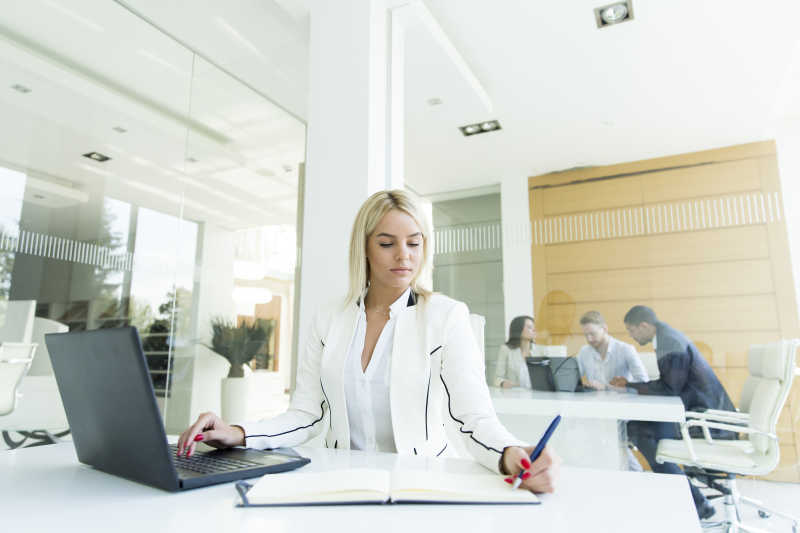 一手拿笔一手摸电脑的办公室女商人